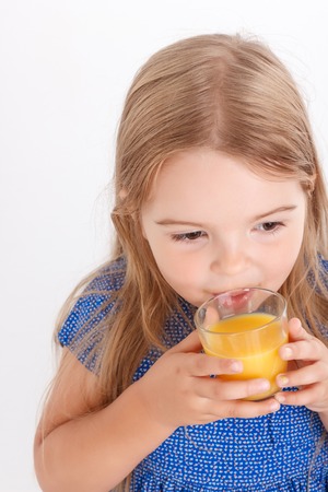I will be healthy. Pleasant cute little girl holding glass and drinking juice while standing isolated on white background.の写真素材