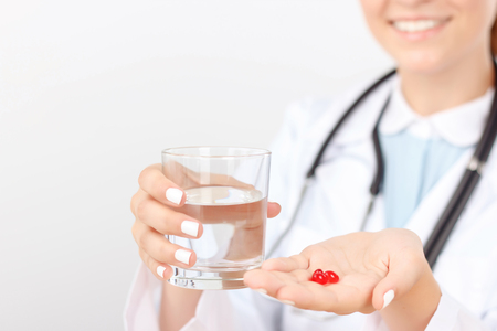 Take it every day. Vivacious  smiling woman doctor holding glass of water and pills giving them to her patient.の写真素材