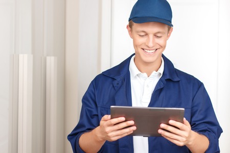 Happy to work here. Cheerful pleasant deliveryman holding laptop and looking down while waiting near the doorの写真素材