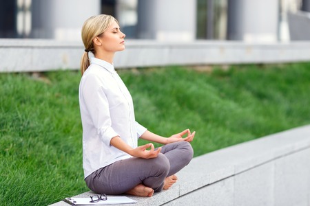 Feel the harmony with nature. Nice charming businesswoman sitting near office building and  practicing yoga while relaxing after hardworking dayの写真素材