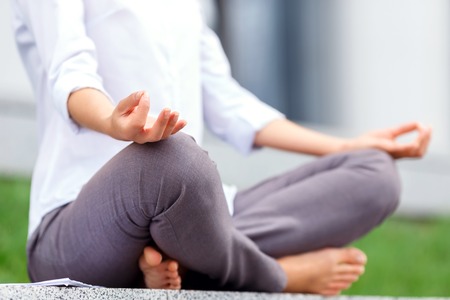 Peaceful moment. Pretty businesswoman practicing yoga  and  relaxing while sitting near office buildingの写真素材