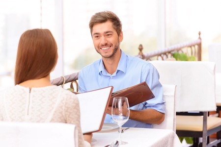 Just feel my love. Nice happy young couple sitting in the restaurant and holding menu while going to spend pleasant evening.の写真素材