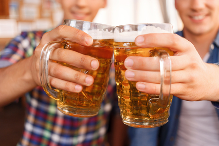 Best beverage. Pleasant upbeat friend holding jugs of beer and going to drink it while relaxing in the pubの写真素材