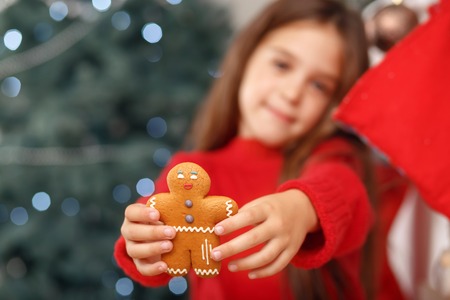 Eat me. Close up of ginger bread in hands of cheerful little girl holding it and expressing gladness.の写真素材