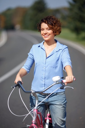 Full of energy. Cheerful smiling active girl holding bicycle and riding it while spending great timeの写真素材