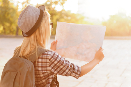 Where should I go.  Nice content young girl holding map and walking around the  city while standing turned backの写真素材