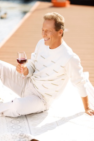 Like it so much. Pleasant delighted adult  handsome man  holding glass and reveling in drinking wine while expressing pleasure.の写真素材
