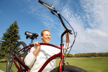 Healthy and strong. Cheerful handsome agreeable man holding bicycle and smiling while feeling elatedの写真素材