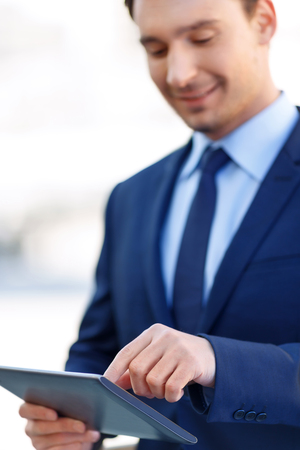 Closer look. Fine-looking young white-collar worker smiles while zooming something on his tablet.の写真素材