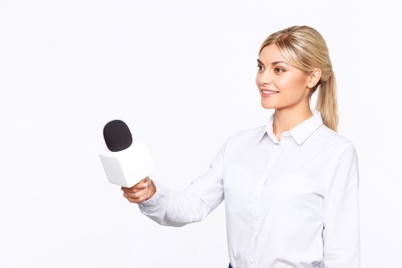 Love doing it. Cheerful content professional Tv announcer holding microphone and interviewing while being busy at workの写真素材