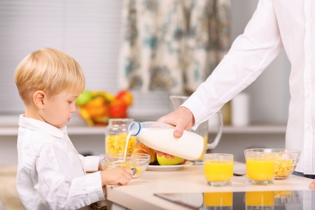 Cornflakes and milk. Dad helps his son with adding milk to the bowlful of cornflakes.の写真素材