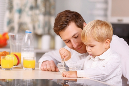 Finish your portion. Caring father gently encouraging his small son to eat up a cereal.の写真素材
