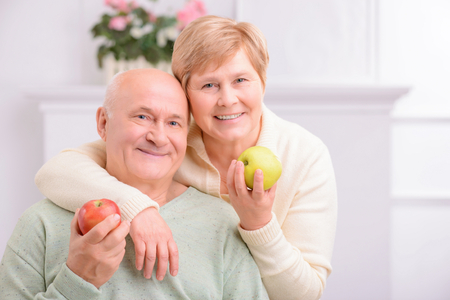 Take care of your health. Agreeable content adult couple holding apples and embracing while resting at homeの写真素材