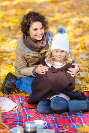 Love you so much. Cheerful content beautiful mother embracing her daughter and sitting with her on the blanket while relaxing in parkの写真素材