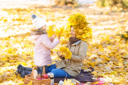 Favorite season. Overjoyed pleasant mother and daughter holding yellow leaves and having fun in park...