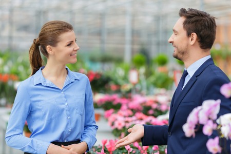 Nice conversation. Pleasant smiling businesswoman talking with her colleague while discussing their business in the greenhouseの写真素材