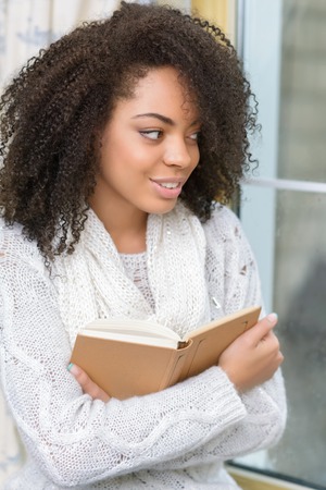 Pleasant evening. Close up of pleasant delighted girl holding book and looking aside while feeling gladの写真素材