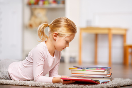 Lovely little girl is lying in fluffy floor carpet and reading.の写真素材