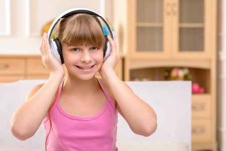 Devoted music fun. Nice smiling positive little girl wearing headphones and holding them by hands while listening songsの写真素材