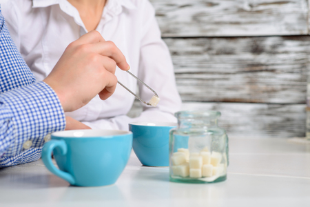 Selective focus of tongs in hands of  handsome positive man holding it and adding sugar to coffee of his female friendの写真素材