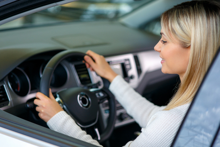 Pleasant cheerful delighted woman sitting at the wheel while choosing auto in auto show and going to buy itの写真素材