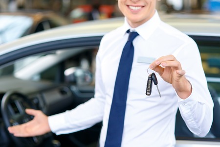 Selective focus of keys in hands of professional smiling sale assistant holding them while showing you the autoの写真素材