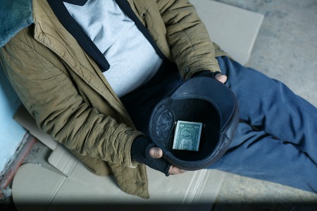 Asking for help. Depressed old beggar is sitting on cardboard and asking for money.の写真素材