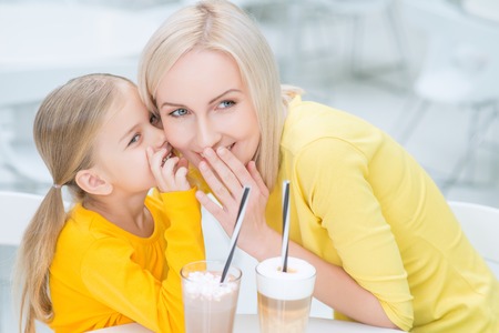 Tell me the secret. Pleasant delighted mother and daughter sitting at the  table and gossiping while resting in the cafeの写真素材