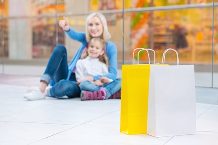 Look here. Selective focus of packages standing on the floor of shopping mall with mother and daughter resting in the backgroundの写真素材