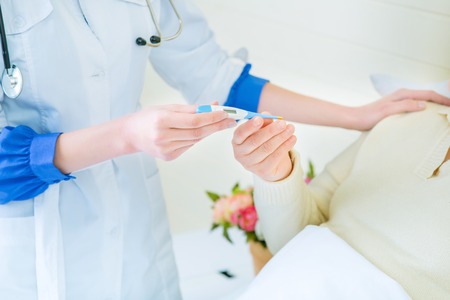 Measure you temperature. Close up of thermometer in hands of professional nurse giving it to her patient while taking care of herの写真素材