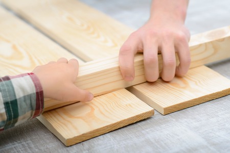 Natural house. Close up of hands of father and his son holding stick of wood while making renovation...