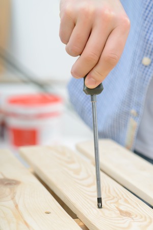 Ready to work. Close up of screwdriver in hands of nice man holding it and working with wood