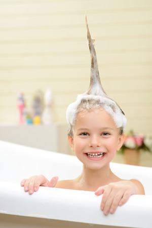 Like the process. Cute little girl sitting in the bath tube and washing her hair while having fun