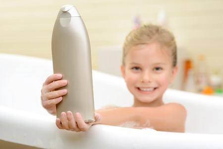 My best helper. Selective focus of bottle of shampoo in hands of little cute girl holding it while...