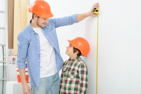 You are so big. Pleasant smiling father holding  tape measure while measuring height of his son while doing renovationの写真素材