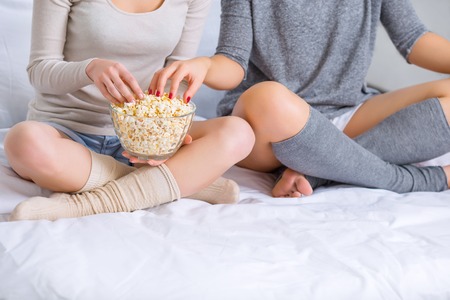 Popcorn included. Two sisters sitting cross-legged and eating popcorn while watching a movie.の写真素材