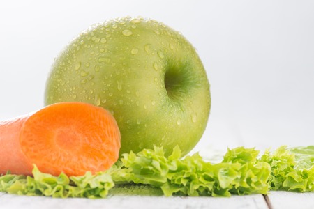 Healthy lifestyle. Close up of  carrot with green apple lying on lettuceの写真素材