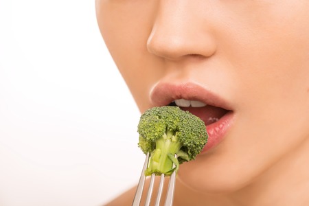 Tasting a broccoli. Young attractive girl is bringing broccoli to her mouth.