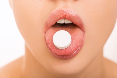 Taking a pill. Young attractive girl is holding a pill on her tongue.