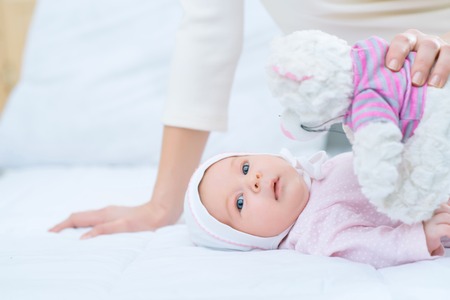 Lets play. Nice little child lying in bed with the nursing mother showing little toy to itの写真素材