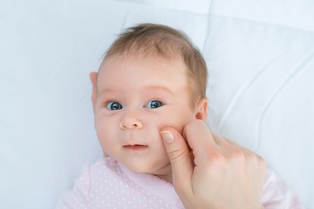 Nice cheeks. Close up of cute infant lying in bed while the nursing mother holding its cheeks.