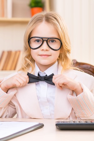Adjusting a tie. Lovely schoolgirl is sitting at the desk and adjusting her bowtie.の写真素材