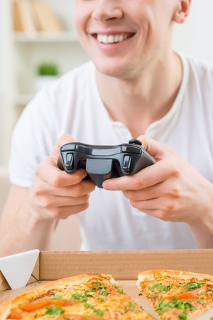 Having fun. Cheerful delighted smiling man holding video game console and playing while expressing gladnessの写真素材