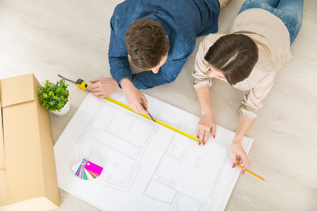 Let it be true. Top view of happy loving young couple holding pencils and drawing plan of their flat while lying on the floorの写真素材