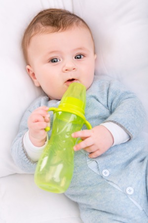 Baby with bottle. Little baby boy is staring funnily while holding his bottle.の写真素材