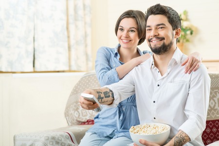 Spend weekend together. Nice smiling positive loving couple watching television and eating pop corn...