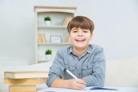 Laughter of joy. Nice joyful kid smiling and making homework attentively with pleasure before school