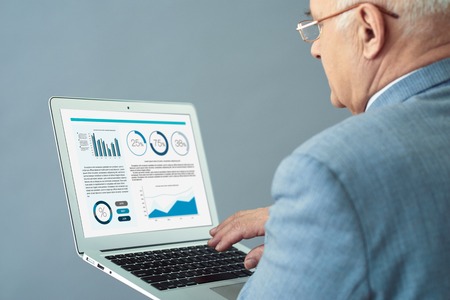 Working atmosphere. Close up shot of experienced old man holding laptop and making up business report.の写真素材