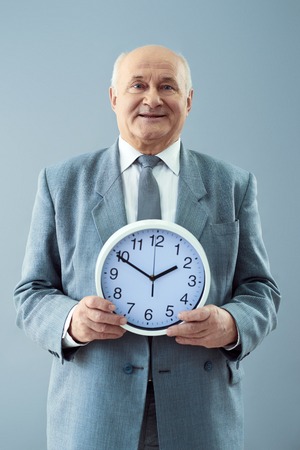 Time management. Studio shot of nice mature man holding a clock and smiling isolated on grey...