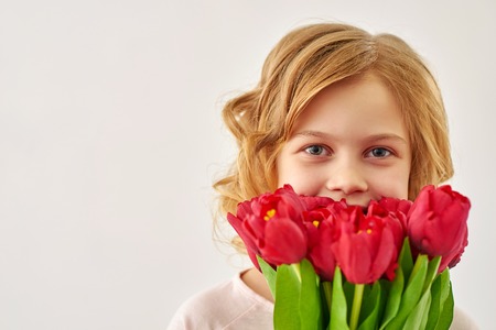 Fresh and cute. Portrait of  lovely blond girl holding  bouquet of tulips against white background.の写真素材